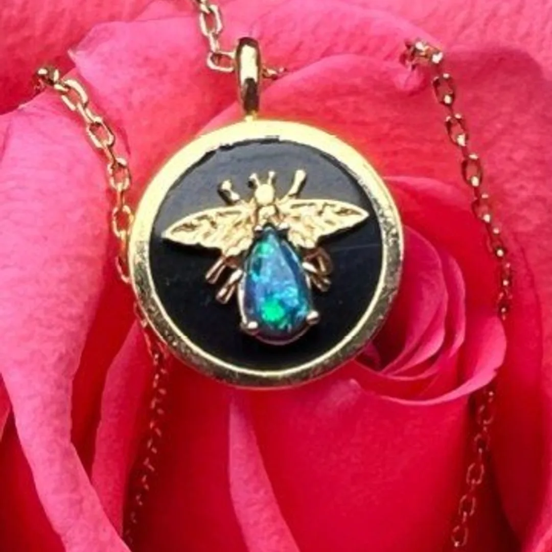 Gold mason-bee pendant on a chain, resting on a pink rose