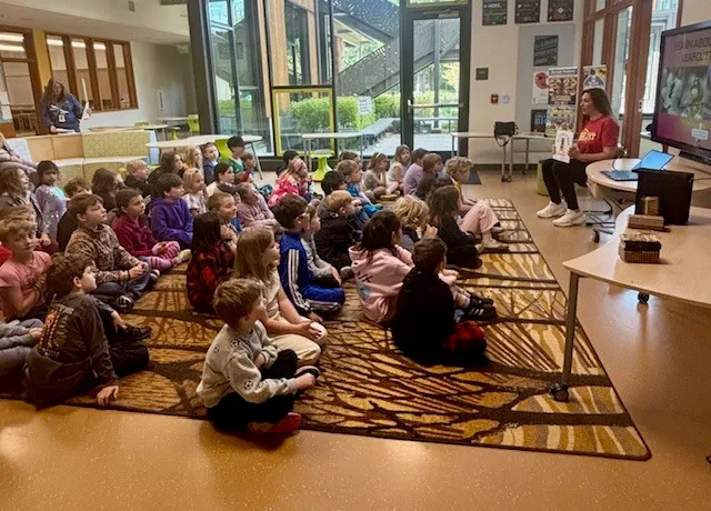 Students sitting on a rug while a teacher leads a mason bee lesson